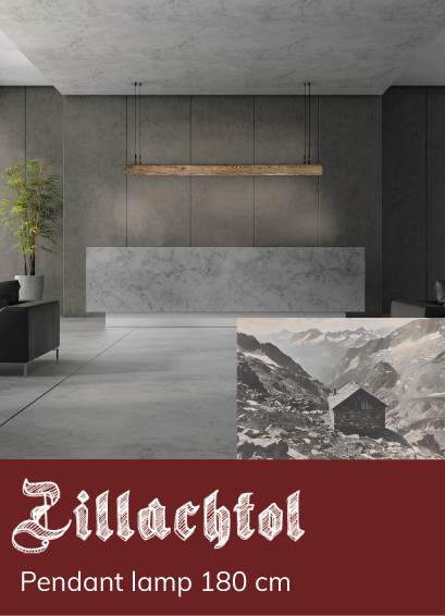 A long, suspended wooden lamp illuminates a modern interior with grey walls and marble elements. Text: &ldquo;Zillachtol pendant lamp 180 cm.&rdquo; In the background, a black-and-white image of a mountain cabin.